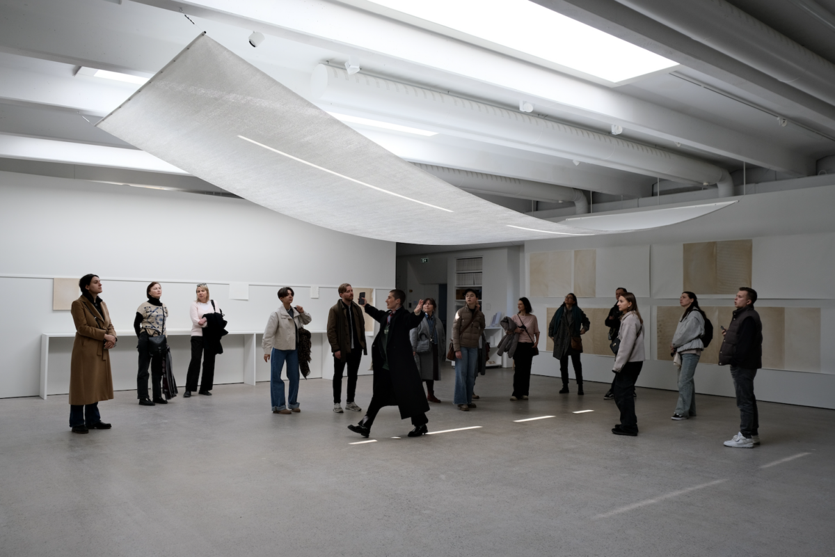 guide with a group of visitors in an exhibition space with a large, white paper work hanging from the ceiling.